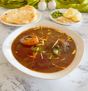 A bowl of spicy curry with meat and chilies served with naan bread and lemon wedges. — Nimona Picture