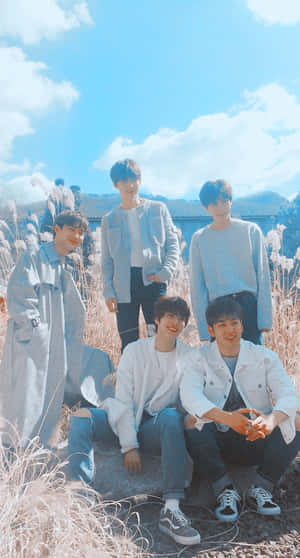 Five young men in light clothing smiling in a sunny grassy field. — Nuest Picture