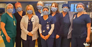 Sieben weibliche Gesundheitspersonal mit Masken und Kitteln posieren für ein Foto in einem Krankenhaus. — Nursery Wallpaper
