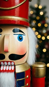 Close-up of a festive wooden nutcracker with blue eyes and white beard near a glowing Christmas tree. — Nutcracker Picture
