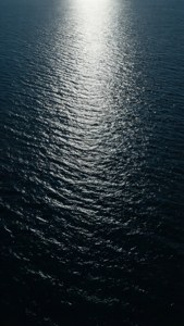 Wallpaper lautan gelap yang tenang dengan pantulan cahaya bulan untuk iPhone.