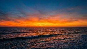 Et fredfyldt fotorealistisk havlandskab, der blander dyb blå himmel med varme orange solnedgangsrefleksioner