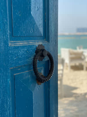 Primer plano de una puerta de madera azul con un llamador de metal negro con vista a una playa. — Divertida pantalla de bloqueo Fondos de pantalla