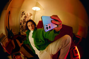 Person in green jacket taking selfie with colorful phone in cozy room.