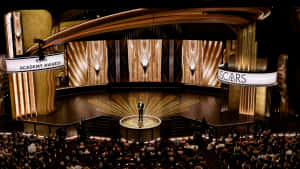 Presenter on Oscars stage with golden backdrop and audience — Oscars Picture