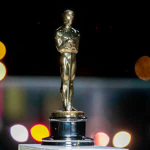 Golden Oscar award statue with blurred colorful lights in background. — Oscars Picture