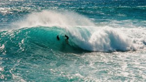 Foto d'azione di un'onda che si infrange nell'Oceano Pacifico con la sagoma di un surfista