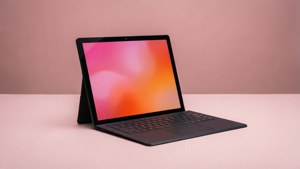 Ein minimalistisches Microsoft Surface mit pink-orangenem abstrakten Verlauf auf dem Bildschirm vor einem pastellrosa Schreibtisch.