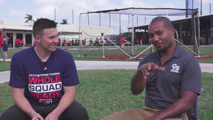 Two baseball coaches talking on grass near batting cage during spring training. — Live Wallpaper