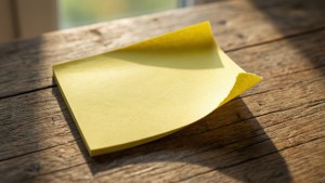 Makrooptagelse af en gul Post-it-seddel, der skræller af på et skrivebord af træ.