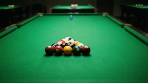 A rack of billiard balls on a green pool table in a dimly lit room. — Snooker Background