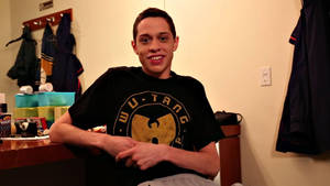 Ung man i Wu-Tang t-shirt ler i stökigt rum med rockar på väggen. — Pete Davidson Bakgrundsbilder