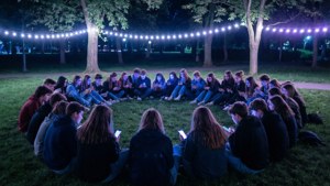 Brat TV panoramisk nattscen med tonåringar i en park upplyst av telefonskärmar och ljusslingor.