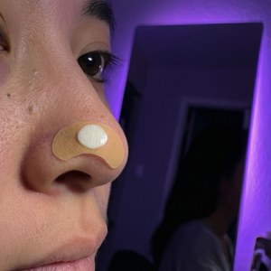 En pimple patch på en näsa i en nattlig hudvårdsrutin med lila neonljus.