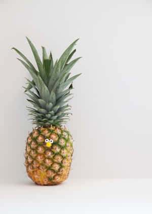 A pineapple with googly eyes and a yellow nose on a white surface. — Cute Pineapple Wallpaper