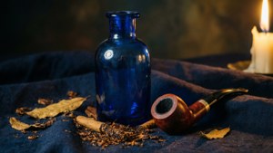 Ein stimmungsvolles Stillleben einer blauen Flasche, Tonpfeife und Tabakblätter im Kerzenlicht.
