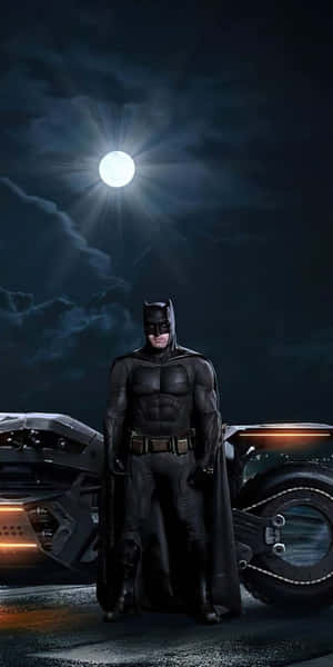 Batman stands beside his Batmobile under a full moon in a dark stormy night.