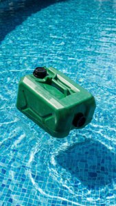 En grön plastdunk flyter i en swimmingpool under starkt solljus, uppfriskande sommarscen.