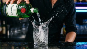Dynamisk actionbillede af bartender, der hælder Tanqueray Gin med splash, neongrøn belysning.