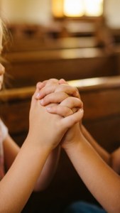 Närbild av barns händer vikta i bön i kyrkan