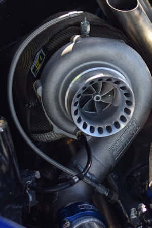 Close-up of a silver turbocharger in a car engine bay with carbon fiber and blue components. — Exact Wallpaper