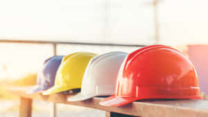 Colorful construction hard hats lined up on a wooden bench in bright sunlight.