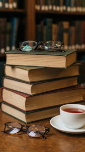 Tumpukan buku yang nyaman dengan kacamata dan teh, estetika perpustakaan preppy yang hangat.