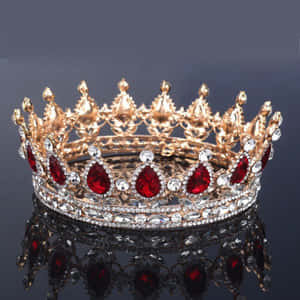 A gold crown with red and clear gems reflecting on a black surface.