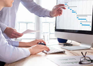 Duas pessoas trabalhando juntas em um computador exibindo um cronograma de projeto. — Gerenciamento de projetos Foto Papéis de Parede