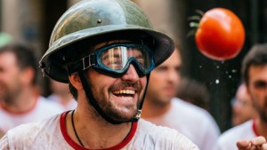 Orang berkacamata pelindung tertawa sambil melempar tomat di La Tomatina.