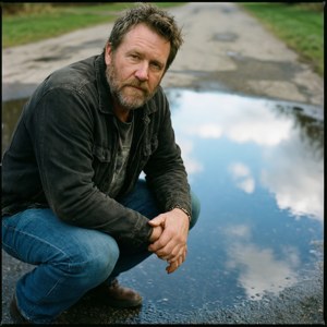 Danny Duncan accroupi près d'une flaque d'eau avec un reflet du ciel.