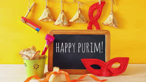 Purim-festartikler inklusive hamantaschen, maske og støjlegetøj på en gul baggrund.
