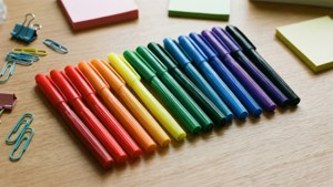 Flad opsætning af Sharpie tuscher i regnbueorden på træskrivebord med kontorartikler.