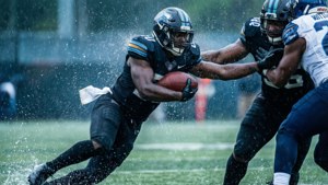Jalen Carter kaster en blokering og rækker ud efter quarterbacken i regnen, med bevægelsessløring og kolde toner.