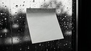 Monokrom bakgrunnsbilde av en hvit Post-it-lapp på et regnvindu med uskarp bakgrunn.