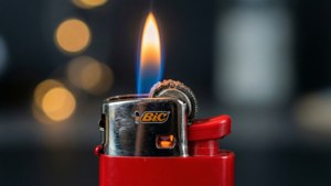 Et makro nærbilde av en rød Bic lighter med en levende flamme mot en bokeh-bakgrunn.