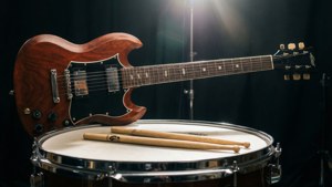 Gibson SG com baquetas em uma bateria no estúdio, contraluz dramática