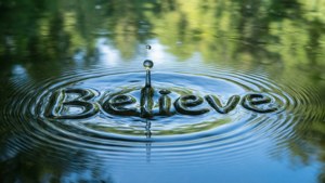 Makro-Hintergrundbild eines Wassertropfens mit 'Believe' in den Wellen