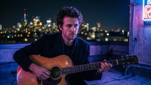 Man playing guitar on rooftop at night with city lights behind him. — Footloose Wallpaper