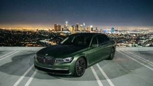 Grüner BMW 7er auf einem Dachparkplatz bei Nacht mit Stadtpanorama.