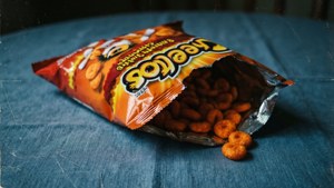 Teilweise aufgerollte Cheetos-Tüte auf blauem Tischtuch, vintage und stimmungsvoll.