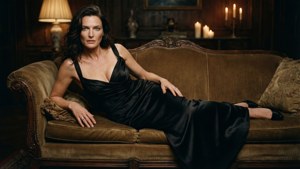 Rachel Weisz i en svart satinklänning, lutad mot en soffa, dramatiska skuggor och levande ljus.