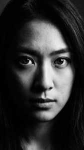Close-up dramatis hitam putih Nikki Hanada dengan pencahayaan tajam.