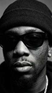 Nærbillede af Skepta i sort hue og solbriller, monokrom