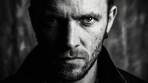 High contrast black and white portrait of Killer Kross with half face in shadow.