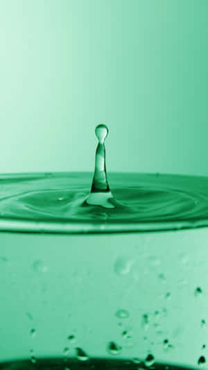 Uma gota de água com tom verde capturada no meio de um respingo acima de uma superfície ondulante. — Estética minimalista Papéis de Parede