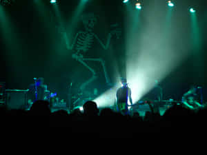 A skeleton projected on stage at a live concert with musicians and a dark audience.