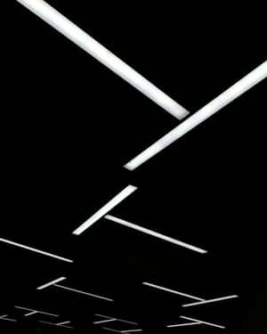 Tubos fluorescentes diagonais contra um teto preto em um ambiente industrial minimalista. — Grunge preto estético Papéis de Parede