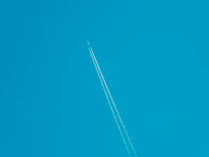 Ett flygplan flyger högt och lämnar två vita spår på en klarblå himmel. — Solid Dark Blue Bakgrundsbilder