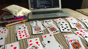 Carte da gioco e laptop su una scrivania di legno con libri e un cuscino nelle vicinanze. — Immagini di solitario Sfondi